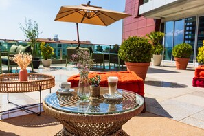 A rooftop terrace with wicker furniture, potted plants, and a glass table with a cup and saucer. - Hotel Tq Plaza (Budva)