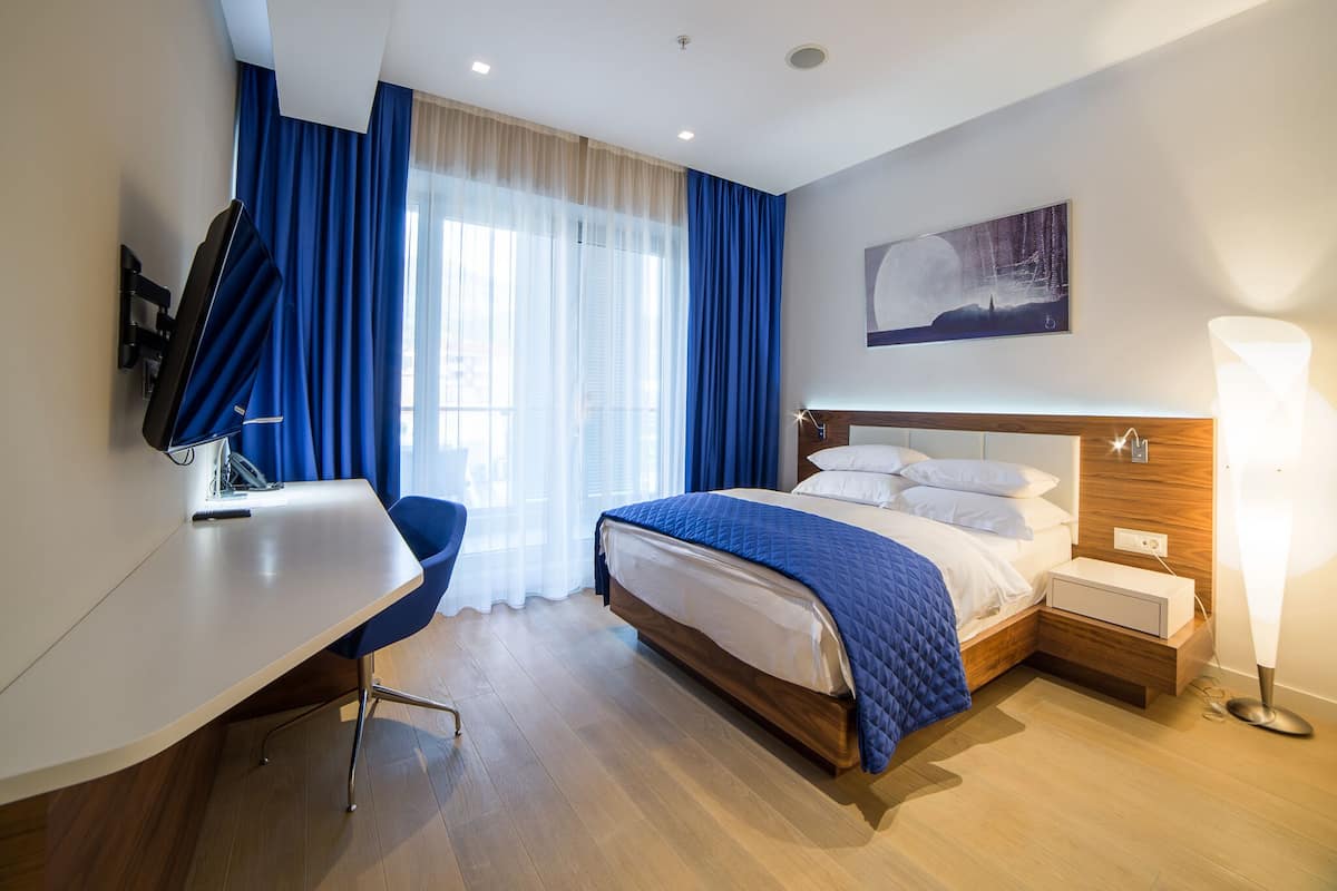 Une chambre d’hôtel équipée d’un lit, d’un bureau, d’une chaise et d’une grande fenêtre avec des rideaux.