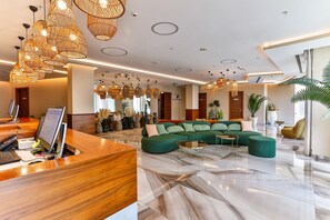 A modern lobby with a reception desk, green sofa, and wicker pendant lights. - Hotel Tq Plaza (Budva)