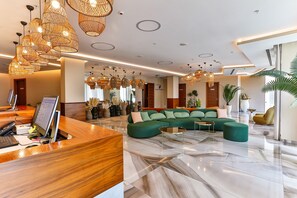 Un vestíbulo moderno con mostrador de recepción, un sofá verde e iluminación colgante de mimbre.