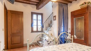 Un dormitorio con cama, armario de madera, ventana con cortinas, escalera y puerta.