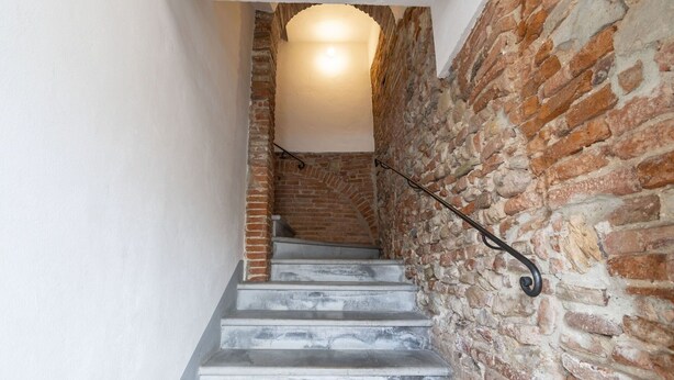 Una escalera con un costado de pared de ladrillo y el otro de pared blanca, que lleva a una zona iluminada en lo alto.