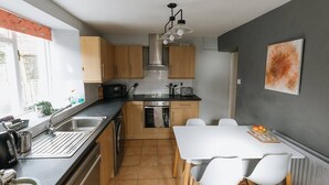 Una cucina moderna con mobili in legno, una cappa aspirante in acciaio inossidabile, un piano di lavoro nero e un tavolo da pranzo bianco con quattro sedie.