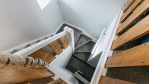 Una scala in legno con corrimano, gradini rivestiti di moquette e una piccola finestra in cima.
