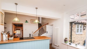 A modern kitchen with a wooden countertop, two pendant lights, a built-in stove, and a view of a stone building through a window. - Riseholme (Scarborough)