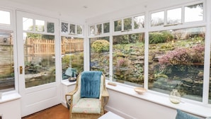 A room with a large window overlooking a garden, a wicker chair, and a white table. - Riseholme (Scarborough)