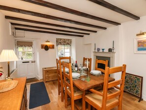 A dining area with a wooden table set for four, surrounded by wooden chairs. A small wooden cabinet and a lamp are visible on the left. - Riseholme (Scarborough)
