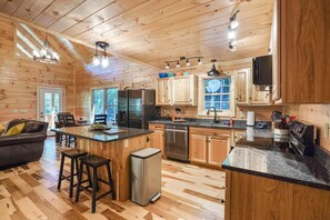 Kitchen features a central island, refrigerator, dishwasher, and sink, with a dining area and large window.