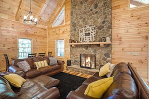Relax by the stone fireplace in this inviting living room, featuring a large leather sofa and wooden ceiling with exposed beams.