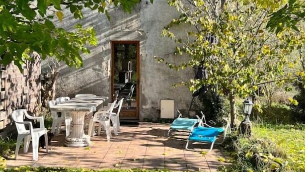 An outdoor patio with a stone wall, a table with chairs, and a door leading to an interior space.