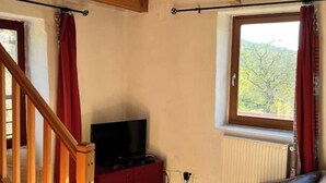 A bedroom with a wooden staircase, a TV on a red cabinet, a window with a view of trees, and a bed with pillows.