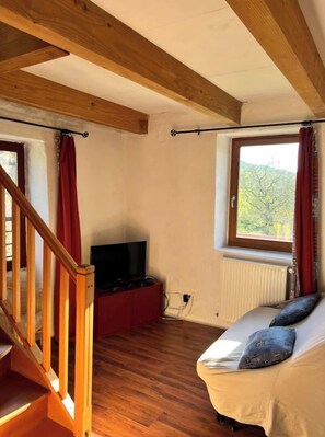 Experience the rustic charm of this cozy retreat, featuring a high ceiling, wooden beams, and a large window with a forest view.