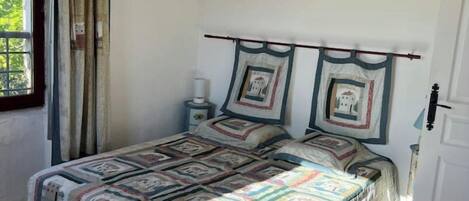 Un dormitorio con una cama grande, vigas de madera en el techo, una ventana con cortinas y una mesita de noche con lámpara.