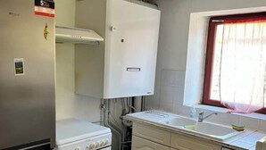A compact kitchen with a refrigerator, oven, white cabinets, a sink, and a window with curtains.