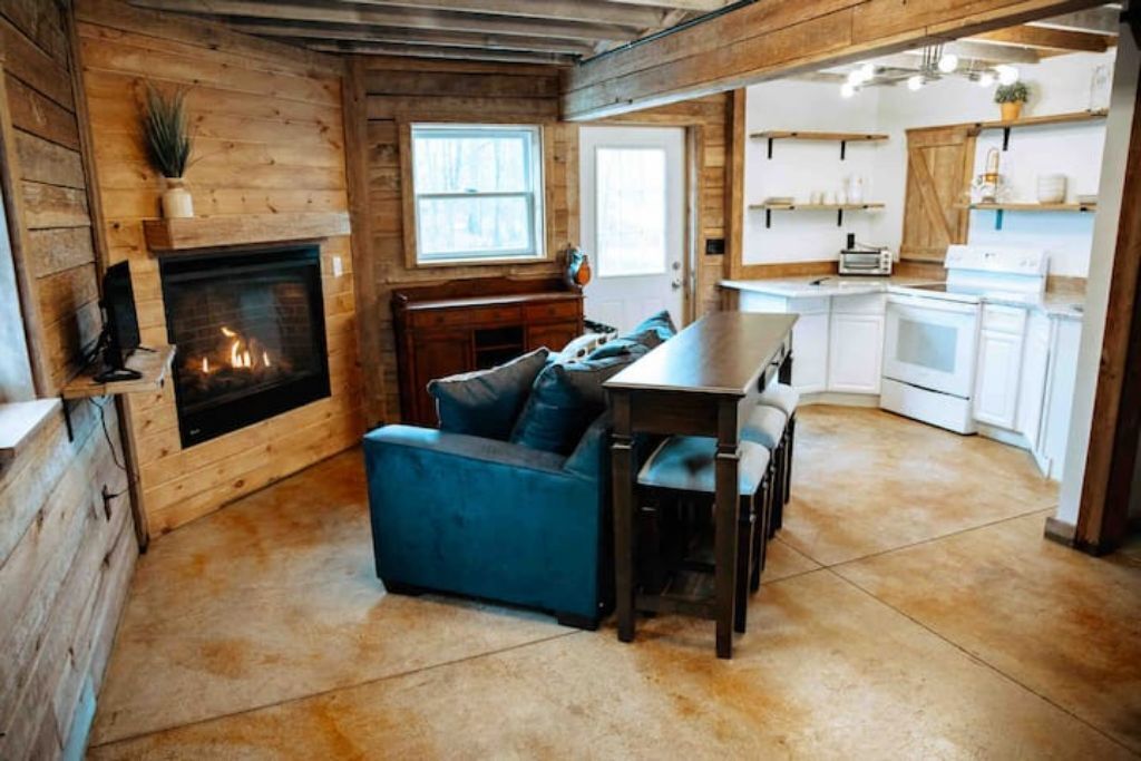 A cozy cabin interior with a fireplace, a blue sofa, a dining table, and a kitchen area.
