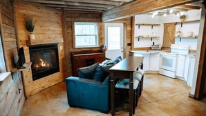 L’intérieur d’un chalet accueillant, avec une cheminée, un canapé bleu, une table à manger et un coin cuisine.