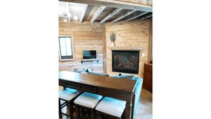 Un intérieur en bois avec une cheminée, une table à manger avec des bancs et un téléviseur fixé au mur.