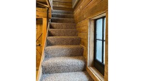 Un escalier en bois, dont les marches sont recouvertes de moquette, mène à une fenêtre.