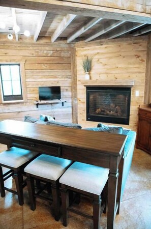 A wooden interior with a fireplace, a dining table with benches, and a TV mounted on the wall.