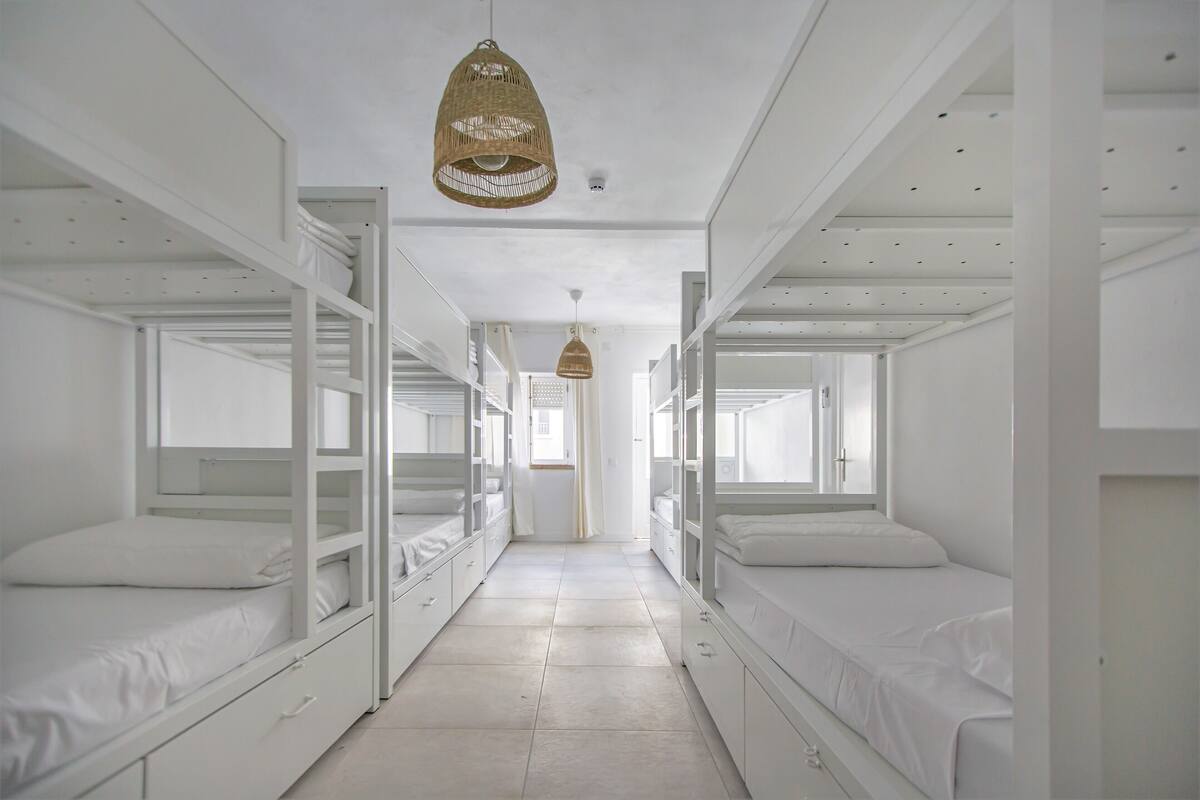 A corridor with bunk beds, white walls, and hanging wicker lamps.