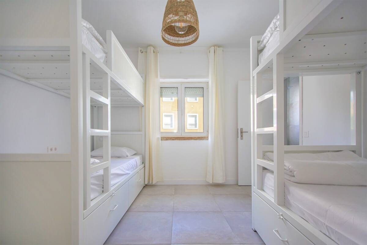 A room with bunk beds, a window with curtains, and a hanging light fixture.