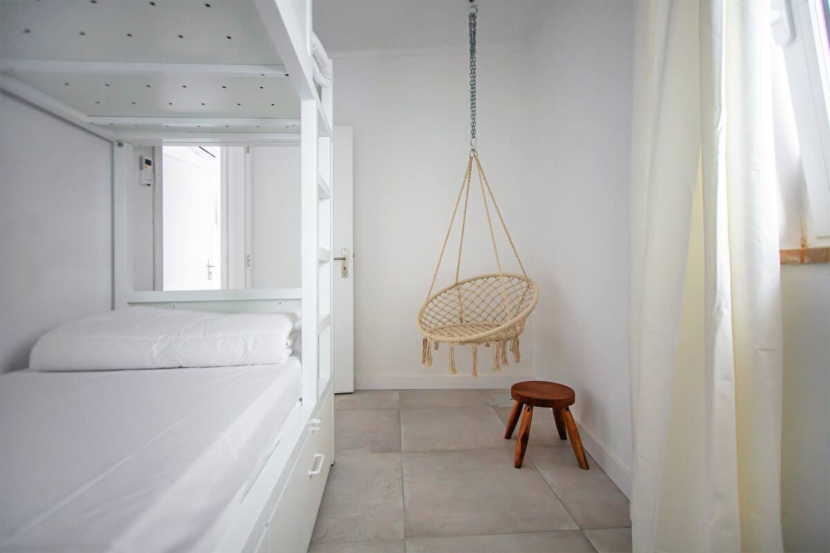 A room with a bunk bed, a hanging chair, and a small stool.
