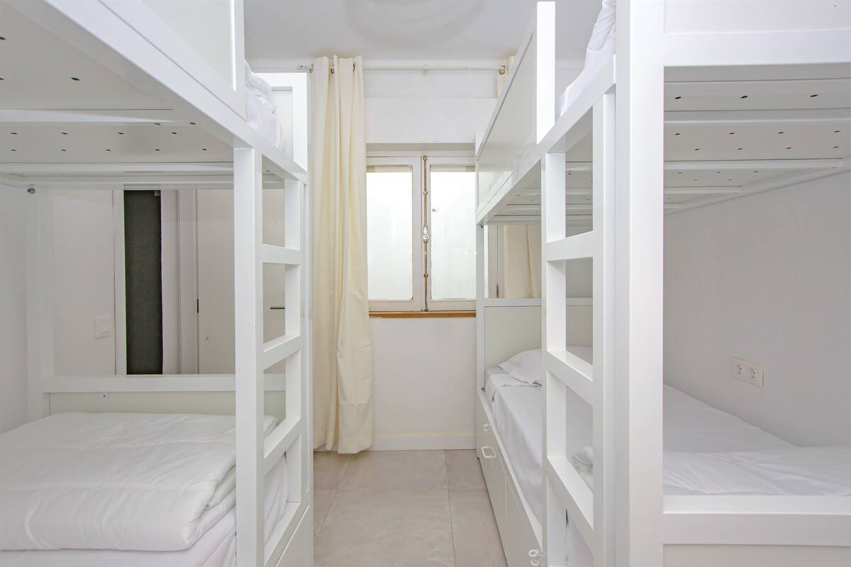 A bunk bed room with a window, curtains, and a door.