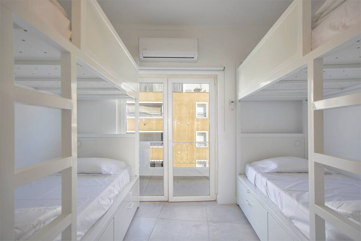 A room with bunk beds, a sliding glass door leading to a balcony, and a ceiling-mounted air conditioner.