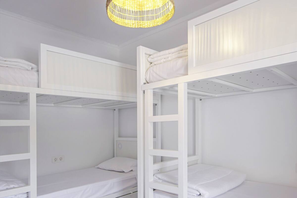 A bunk bed room with white bedding and a woven light fixture.