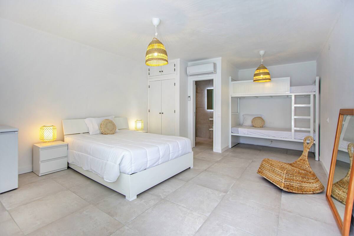 A bedroom with a bed, nightstands, a hanging lamp, a woven basket, and a bunk bed.