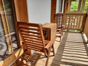 Une terrasse en bois avec une table et des chaises, une porte vitrée et une vue sur la verdure.