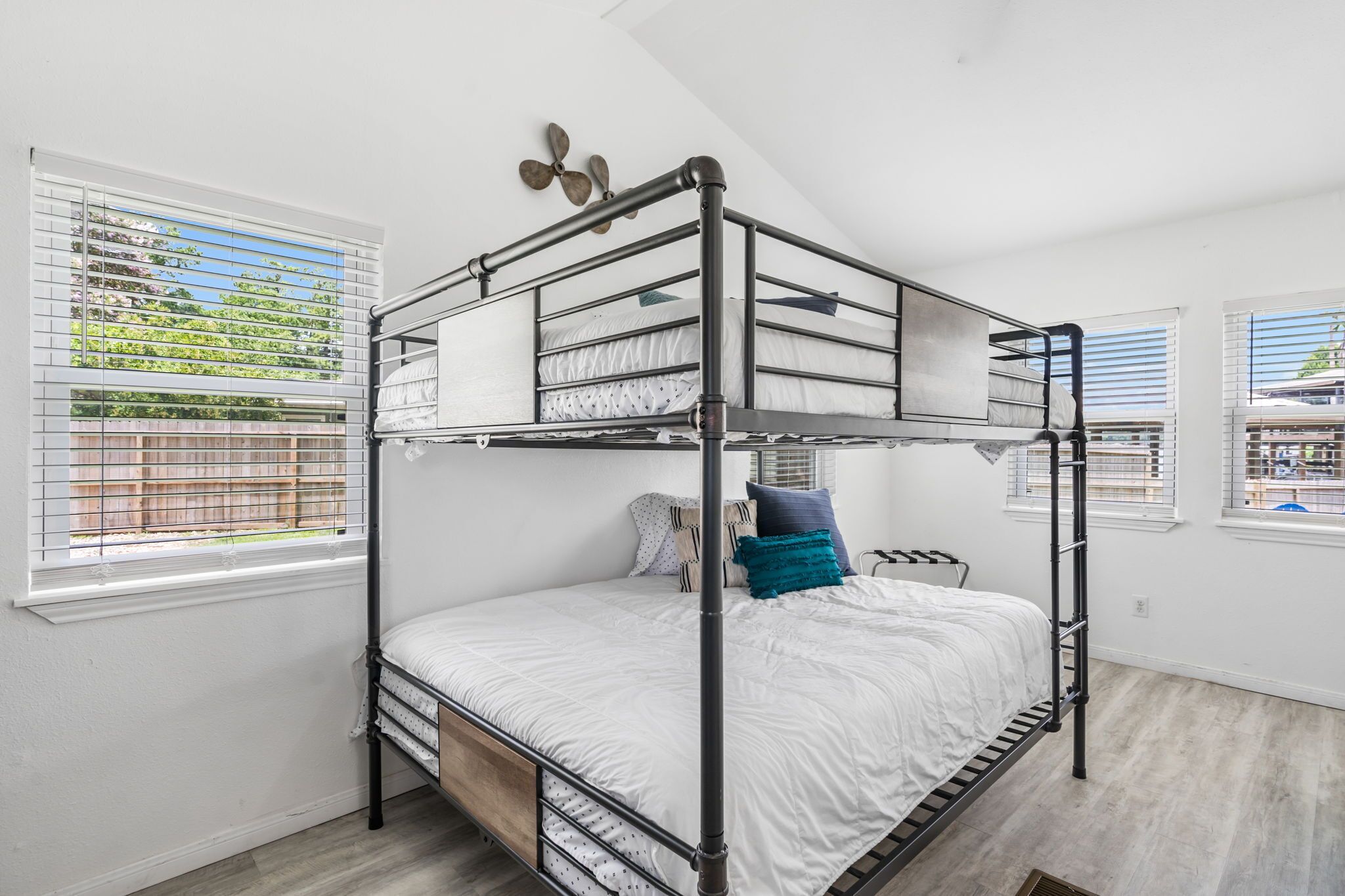 A bunk bed room with a window view of a garden and a ceiling fan.