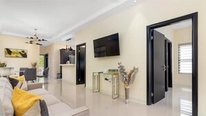 Ein modernes Wohnzimmer mit einer Couch, einem an der Wand montierten Flachbildfernseher und einem Essbereich im Hintergrund.