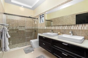 Un baño moderno con ducha de vidrio, dos lavamanos y un espejo grande.