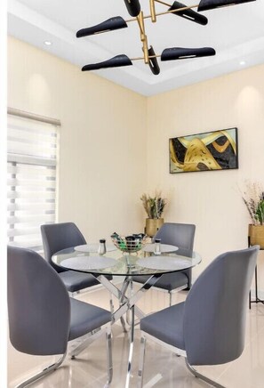 Un comedor moderno con una mesa redonda de cristal, sillas tapizadas en gris y una lámpara de araña contemporánea.