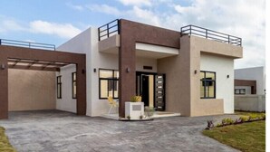 Ein modernes, zweistöckiges Haus mit flachem Dach, einer überdachten Terrasse und einem kleinen Garten.