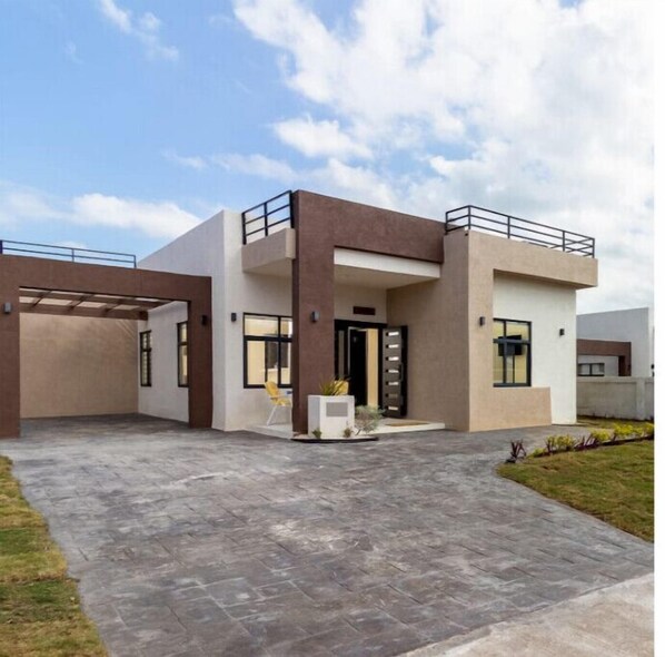 Una casa moderna de dos pisos con techo plano, un porche cubierto y un pequeño jardín.