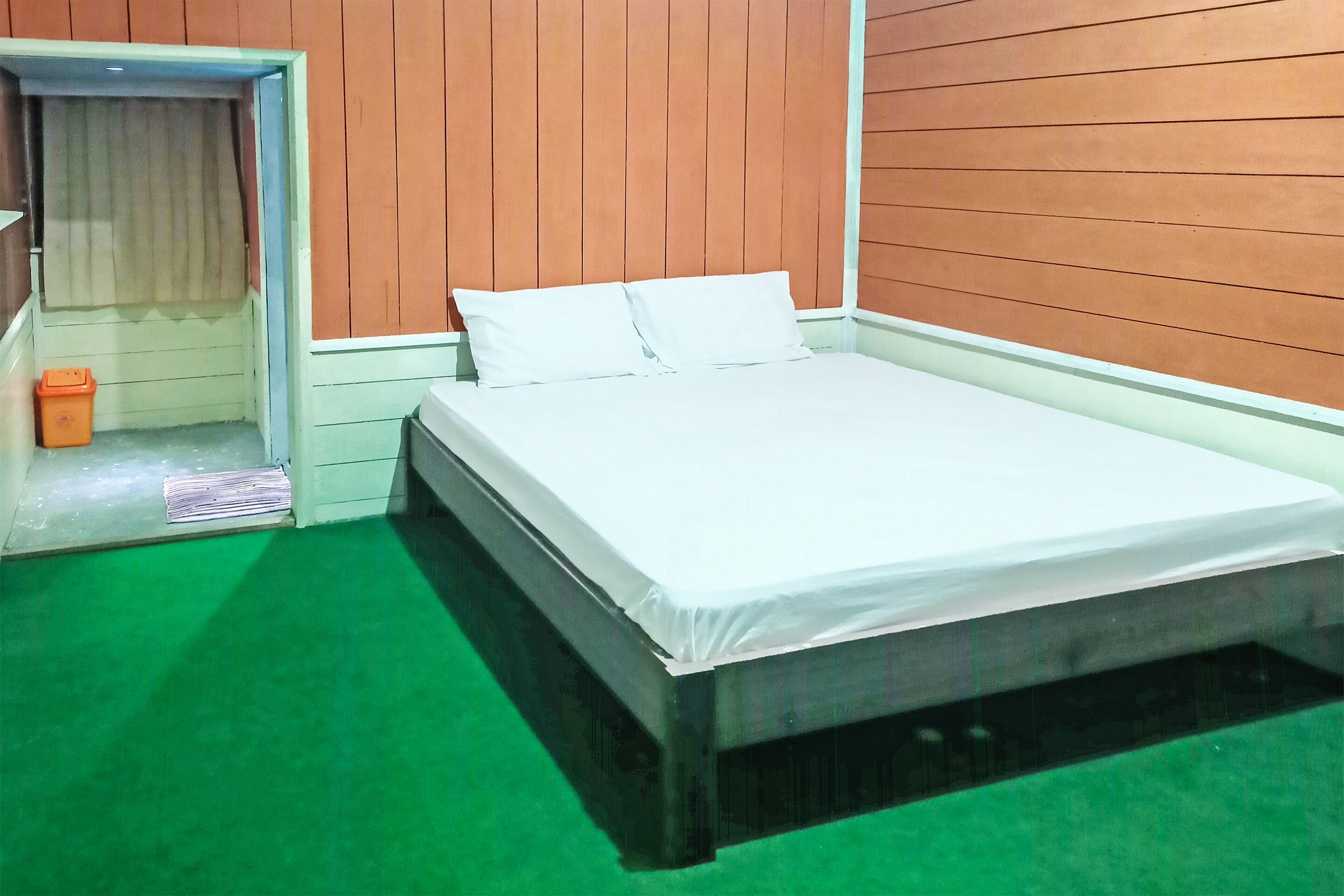 Una habitación con una cama, un cesto de basura pequeño y una puerta que da a otra habitación.