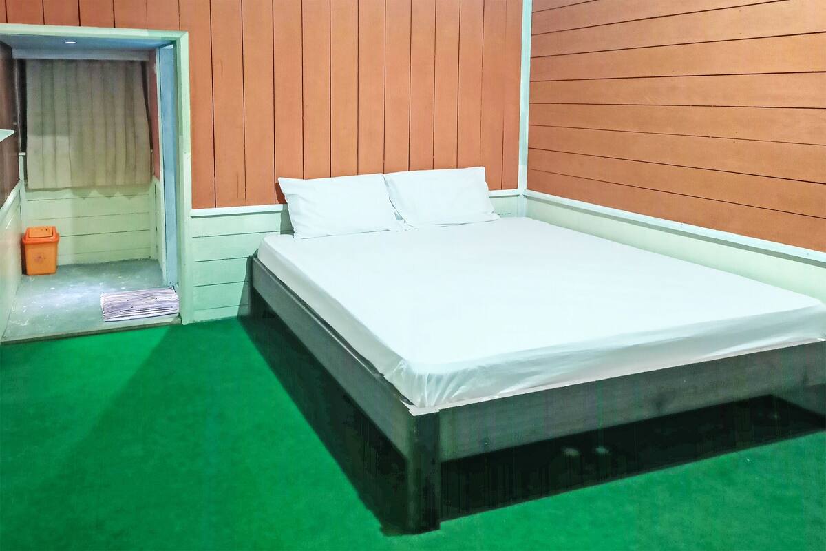 Una habitación con una cama, un cesto de basura pequeño y una puerta que da a otra habitación.