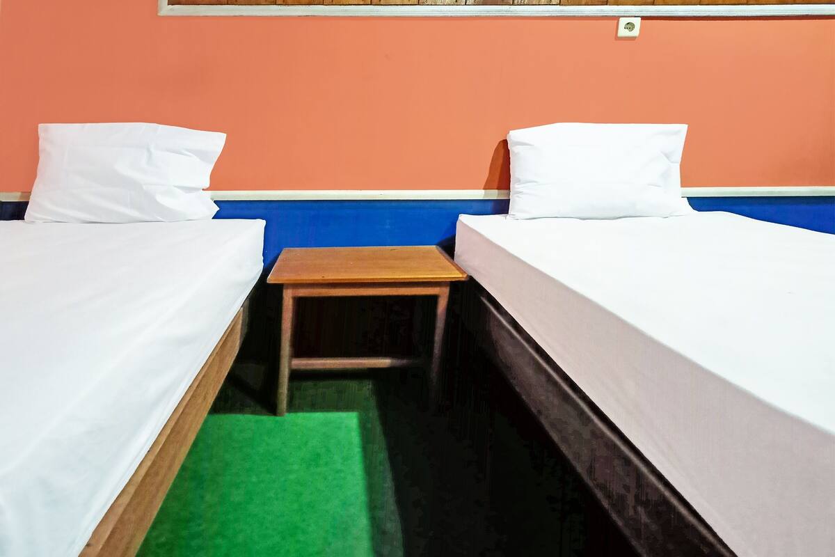 Una habitación con dos camas individuales, cada una con ropa de cama blanca, una mesita de madera y una alfombra verde.