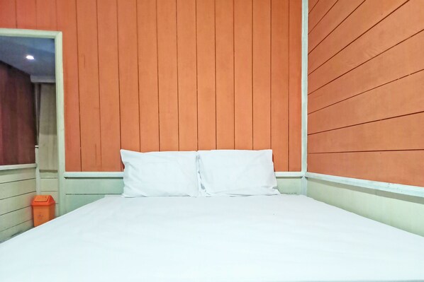 A bed with white bedding, a wooden headboard, and an orange trash bin.