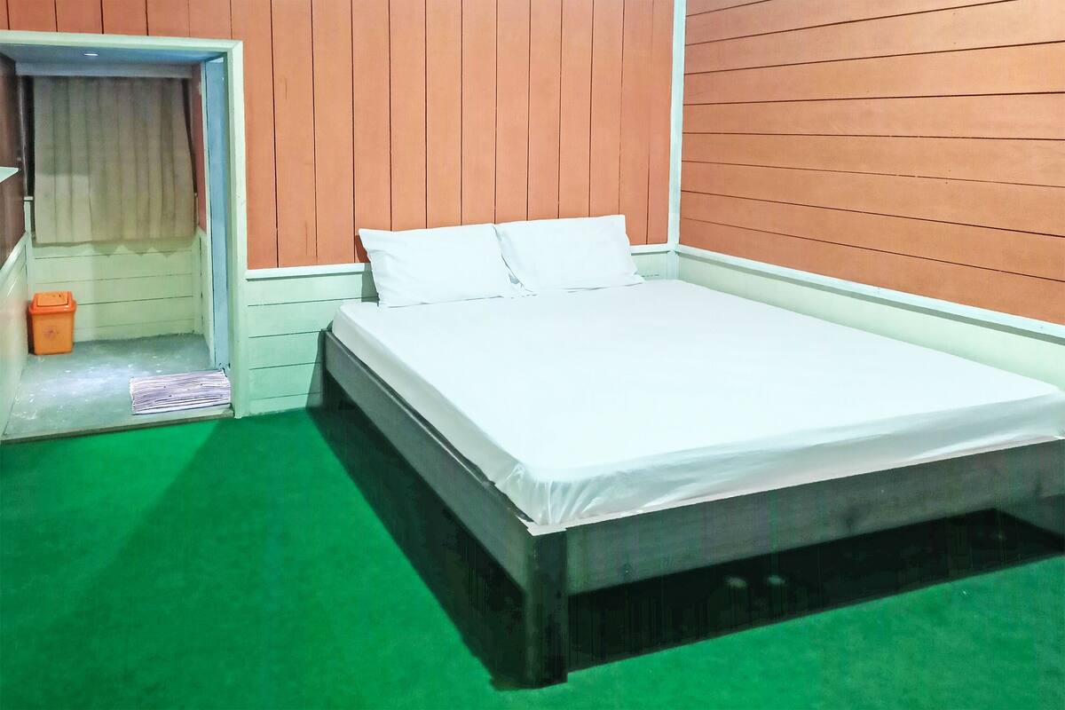 Un dormitorio con una cama, paredes de madera y una alfombra verde.