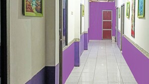 A hallway with purple walls and white doors, leading to a room with a red door. - OYO 91768 Hotel Tanjung Permai (Tanjung Selor)