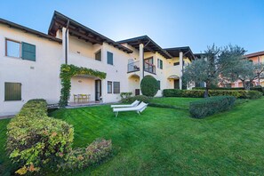 A multi-story building with a well-maintained lawn, two lounge chairs, and a small patio area. - Le Giare PT 7 by Wonderful Italy (Polpenazze del Garda)