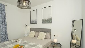 Ein Schlafzimmer mit einem Bett, Nachttischen, einer Lampe, einem Spiegel und Bildern an der Wand.