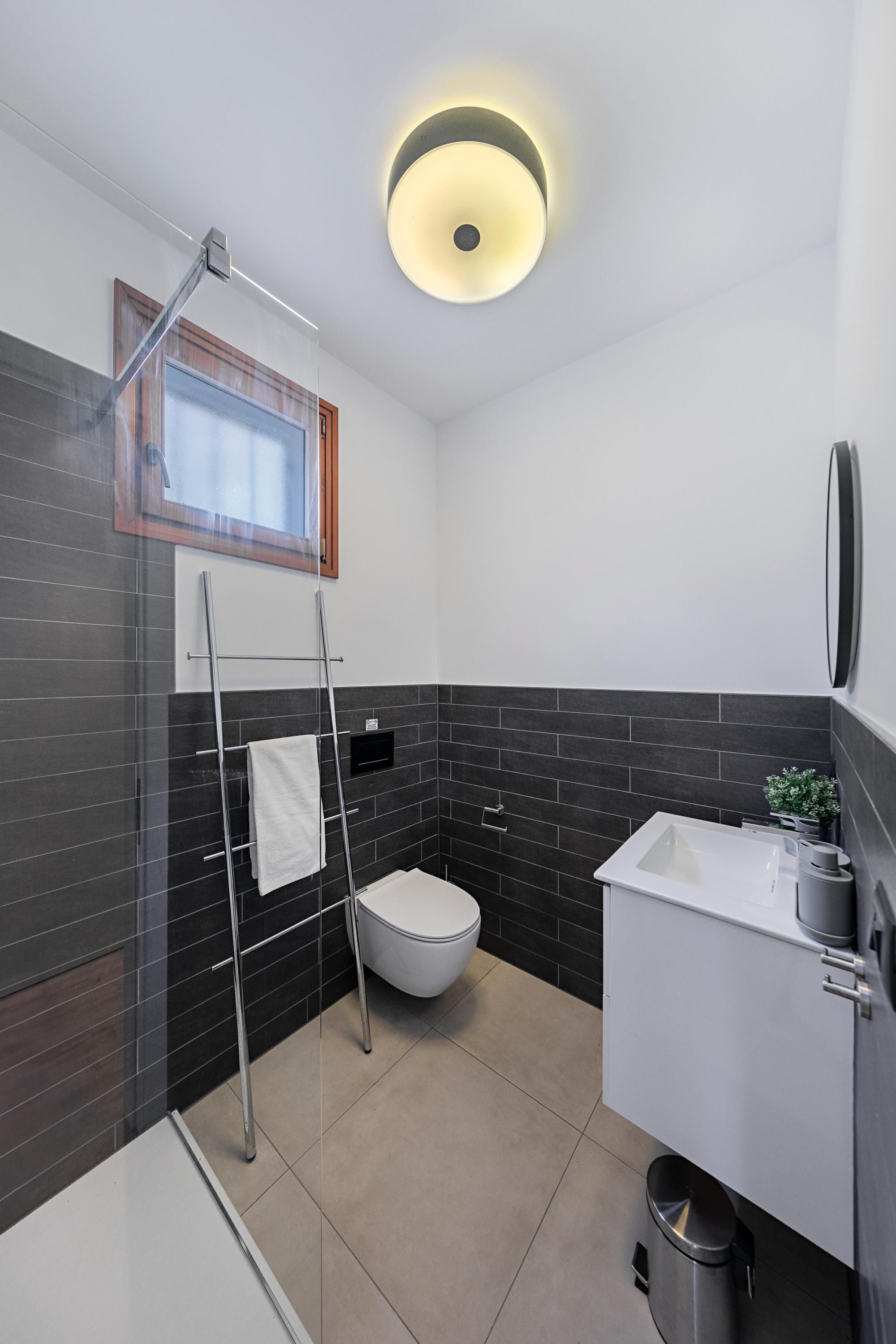 A modern bathroom with a glass shower enclosure, a white toilet, a white sink with a plant, and a black and white tiled backsplash.