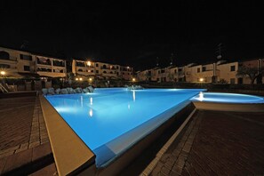 A rectangular swimming pool with a smooth surface, surrounded by a paved area and a row of buildings with multiple stories and balconies. - Le Giare PT 7 by Wonderful Italy (Polpenazze del Garda)