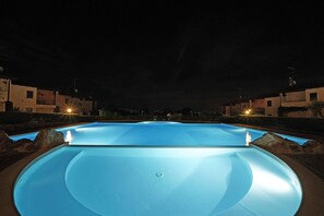 A swimming pool at night with surrounding buildings and streetlights. - Le Giare PT 7 by Wonderful Italy (Polpenazze del Garda)