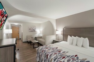 Una habitación de hotel con cama, escritorio, silla, sofá y televisor fijado a la pared.