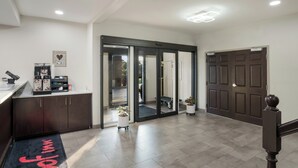 A hotel lobby with a reception desk, a coffee station, a sliding glass door leading to a room, and a dark wooden door. - Red Roof Inn & Suites Carrollton, Ga-west Georgia (Carrollton)